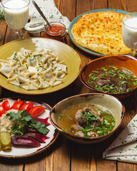 Meat soup with broth, dumplings, a generous table of Georgian dishes. On a wooden table.