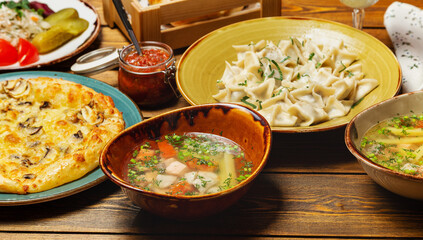 Meat dumplings, soups, appetizers, a generous table of Georgian dishes. On a wooden table.
Horizontal.