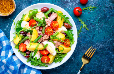 French gourmet salad with tuna, tomatoes, eggs, beans, potatoes and olives on blue background, top view