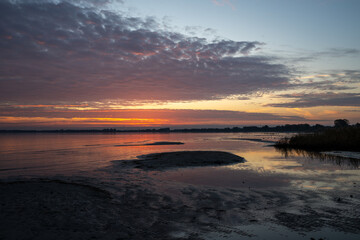Die Sonne durchbricht mit rotem Licht die Wolken und spiegelt sich im Wasser