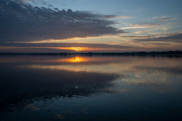Die Sonne durchbricht mit rotem Licht die Wolken und spiegelt sich im Wasser