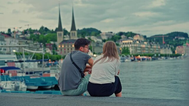 Couple sitting on the shore of Lake Lucerne with the city of Lucerne in the background in summer, Switzerland