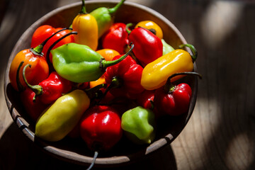 Bowl of colorful pimento peppers, a mainstay of Caribbean cuisine, on a wooden table with dappled light