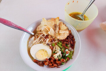 Bubur Ayam, a traditional Indonesian food consisting of white rice porridge, shredded chicken, cakwe, fried soybeans, crackers, green onions and eggs.