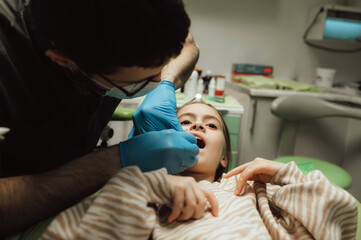 Cropped portrait of little girl with pigtails hair sitting in dental chair looking at camera. A...