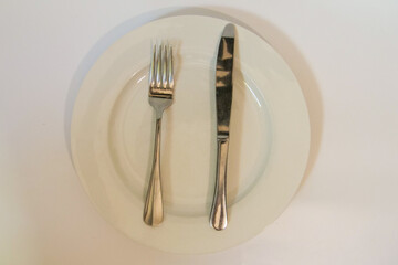 Silver knife and fork on a white porcelain plate on a white background.