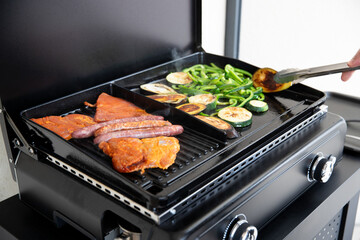 Gros plan sur une main qui grillent de la viande et des légumes sur une plancha. Viande de porc et légumes à l'huile d'olive.