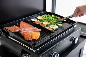 Gros plan sur une main qui grillent de la viande et des légumes sur une plancha. Viande de porc et légumes à l'huile d'olive.