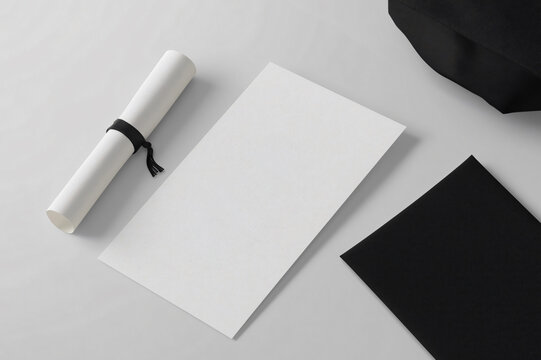 Customizable graduation invitation card mockup is laying on white table next to diploma and black envelope