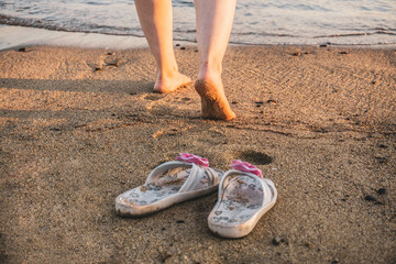 A pair of bare feet leaving footprints on the sandy beach as the waves gently touch the shore.