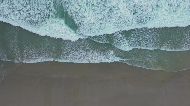 Aerial View Of Foamy Sea Water Splashing On Sandy Beach At Playa de Caion In A Coru&ntilde;a, Spain. top-down, slow-motion shot