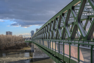 Side view of a green steel bridge crossing a river under a partly cloudy sky.
