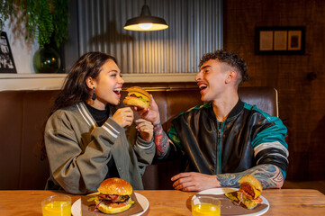 Young man and woman sharing a burger in a restaurant, enjoying a meal together
