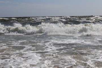 Crashing ocean waves create a dynamic and energetic seascape, with white foam and sparkling water under a clear blue sky, evoking the beauty and power of nature.
