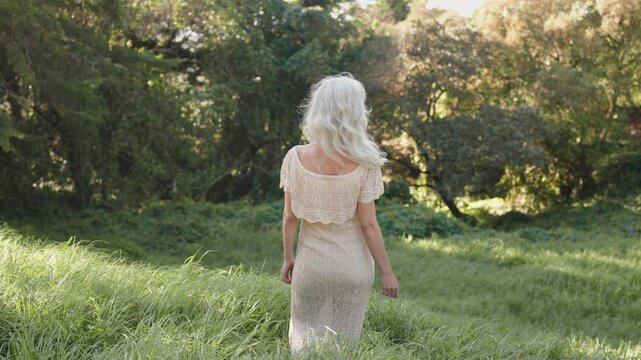 Serene woman with long white hair walks through a field. Ideal for themes of peace, nature, beauty, and aging gracefully.