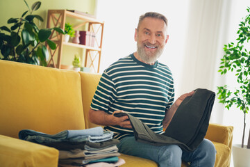 Elderly man enjoying his time at home, folding laundry and smiling in a cozy living room. Capturing everyday joy and contentment.