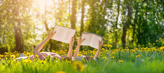 Mother and her child lying down on the green field with blooming flowers and reading books.