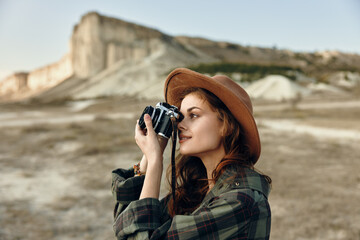 Stylish woman in plaid shirt and hat capturing a moment with vintage camera on sunny day