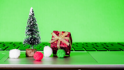 Small holiday decorations on a laptop keyboard with a green background during festive season preparations