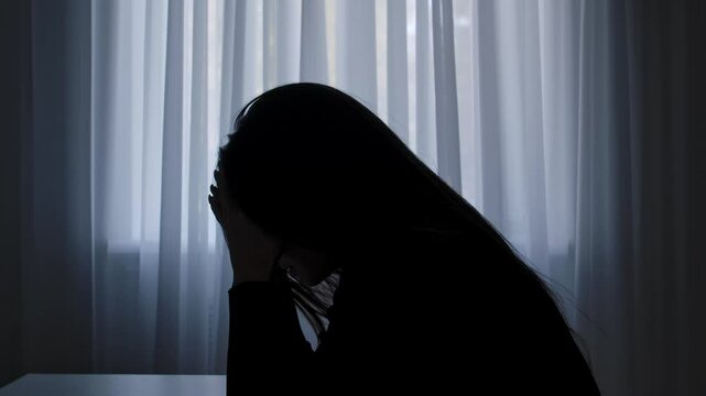 Silhouette of woman sitting at table in front of window. lays head on desk, depressed heartbroken expression, lonely and doubtful. Human emotions and mental health.