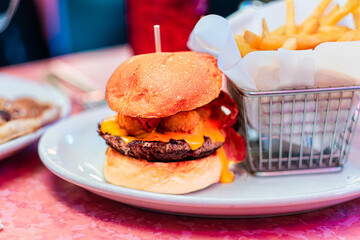 Delicious Cheeseburger and Crispy Fries Served on a White Plate at a Classic American Diner with a Vibrant Pink Tabletop Setting, Highlighting Juicy Beef and Melted Cheese
