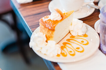 Appetizing Slice of Cheesecake with Whipped Cream and Caramel Sauce on a Plate in a Cozy Cafe Setting