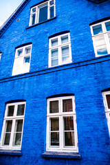 Vibrant Blue Facade of Urban Brick Building Featuring Multiple White Framed Windows Against a Bright Sky