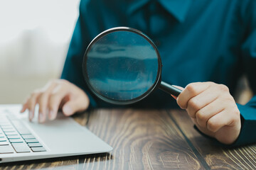 Fototapeta premium person examining laptop with magnifying glass, showcasing focus and attention to detail. setting suggests workspace or study environment