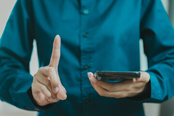 person in blue shirt holds smartphone while gesturing with one finger raised, indicating pause or...