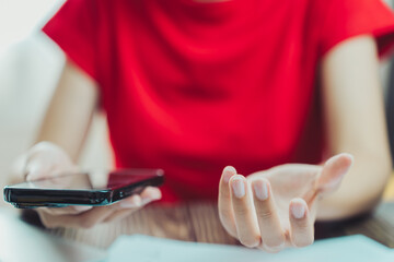 Fototapeta premium person in red shirt is holding smartphone while gesturing with their hand, expressing frustration or confusion. setting appears to be indoor environment, possibly office or home