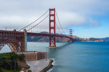 The Golden Gate Bridge spans San Francisco Bay with Fort Point at its base. The International Orange bridge contrasts with blue water and Marin hills.