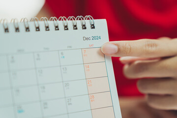 December 2024 calendar with highlighted Saturday date, showing 7th. person points at date,...