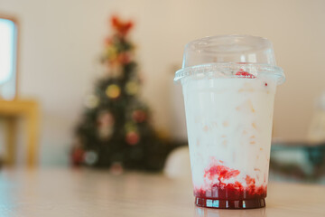 Creamy dessert drink in clear cup with red syrup, festive background
