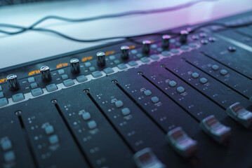 A detailed view of an audio mixing console with sliders and knobs, illuminated by ambient lighting....