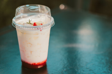 Creamy beverage in clear cup with ice and strawberry topping, placed on dark surface. refreshing drink is perfect for warm days
