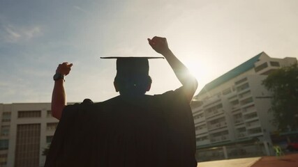 A person in a graduation gown is holding their fist up in the air. Concept of accomplishment and pride, as the person has just graduated from school - Powered by Adobe