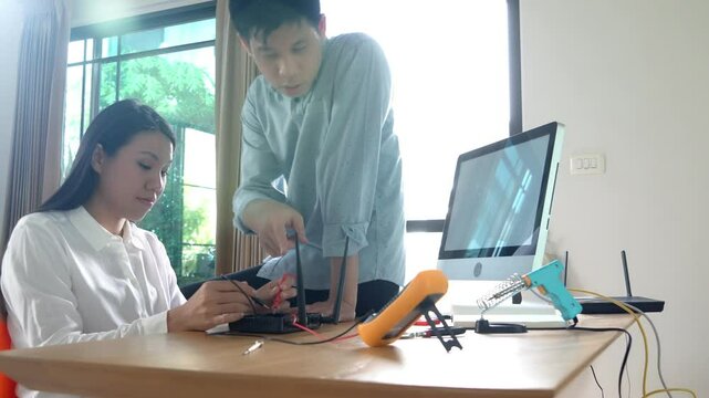 A man and a woman are working on a project together. The woman is holding a tool and the man is looking at a computer monitor. Scene is collaborative and focused