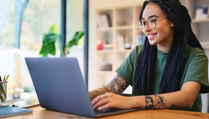 Fototapeta premium Creative young LGBT woman working on laptop. Girl with tattoo, designer freelancer or student work on computer laptop at table