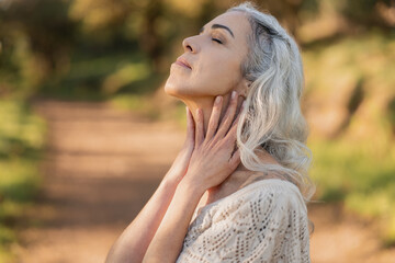 Elderly woman enjoys a peaceful moment in nature, embracing mindfulness under the warm glow of sunset. Her relaxed expression signifies tranquility and fulfillment.