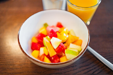 Colorful Fruit Salad in a White Bowl Accompanied by a Refreshing Glass of Orange Juice on a Wooden Table Surface