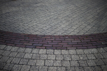 Close-up of a curved brick border on a paved walkway.  Gray paving stones meet a band of reddish-brown bricks.