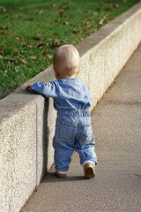 A toddler learning to walk near a pavement edge on a sunny day, symbolizing growth, determination, and early childhood milestones.