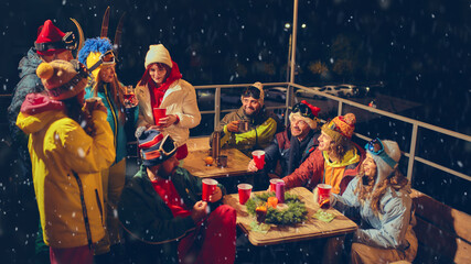 Snowy evening celebration with friends in vibrant ski outfits, raising red cups and enjoying festive gathering filled with laughter and warmth. Concept of holidays, Christmas party. Ad