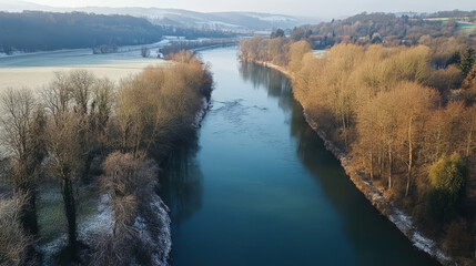 The river flows smoothly, its surface partially frozen in some areas, with patches of ice and snow along the edges