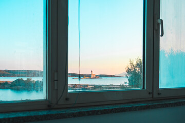 Serene Ocean View Through a Window with Lighthouse in the Distance During a Calm Sunset Evening