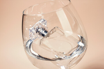 Perfume bottle in a glass with water on a light background