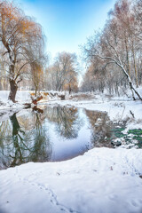 Breathtaking landscape in city park with snowy trees and beautiful reflection in frozen river.