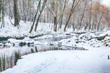 Picturesque landscape in city park with snowy trees and beautiful reflection in frozen river.