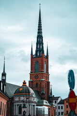 Fototapeta premium Historic Brick Church Architecture with Gothic Spires Under Cloudy Sky in Urban Setting, Showcasing Timeless European Design and Religious Heritage Amidst Modern Cityscape Elements