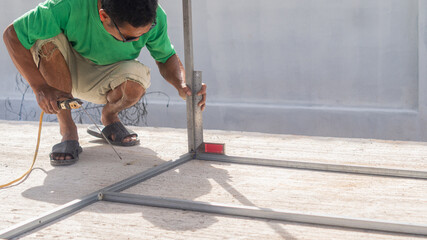 Worker measures angle of steel with right angle ruler before welding, worker makes metal structure in construction site